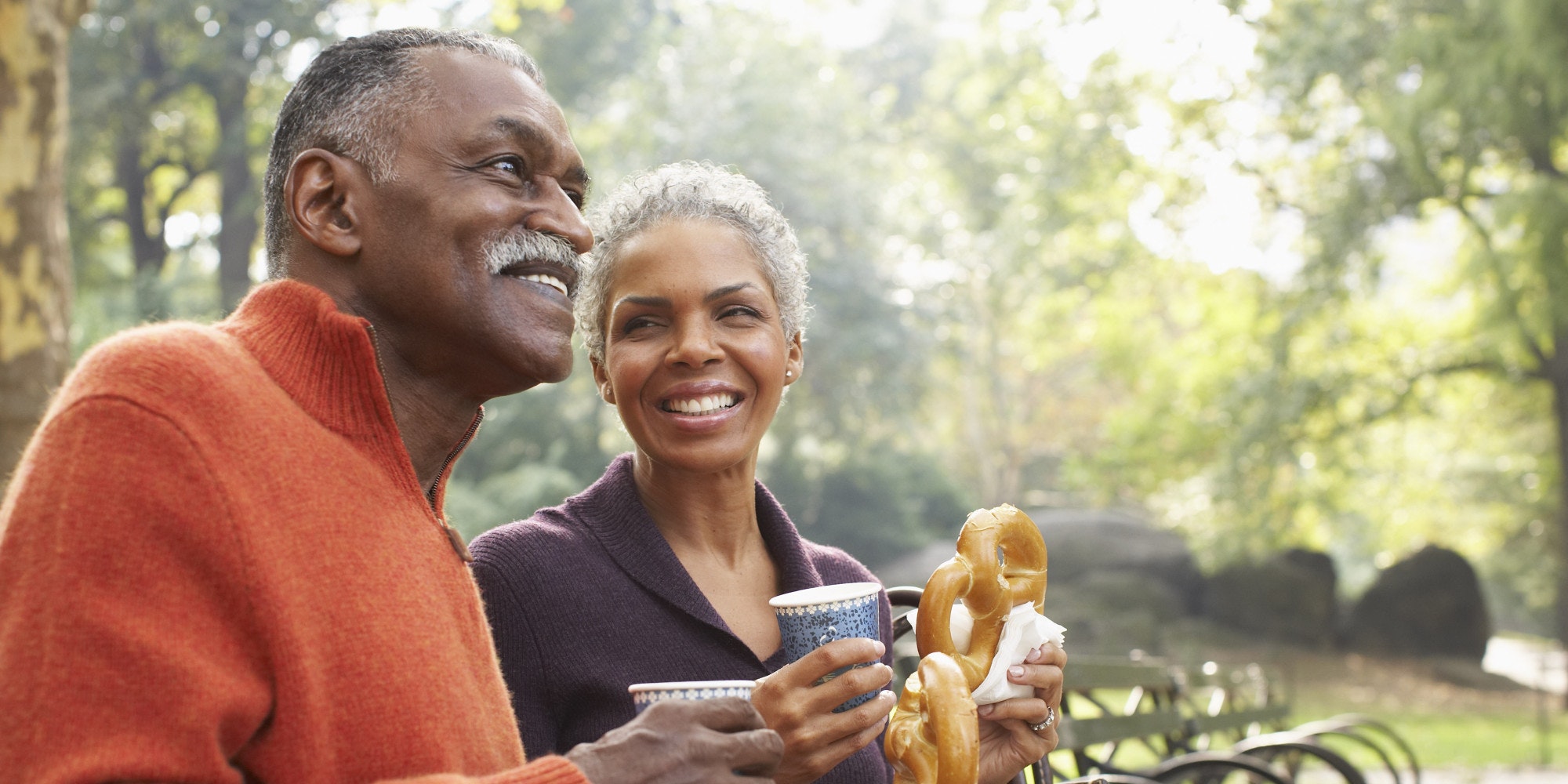 Smiling couple enjoying coffee and a pretzel in a park
